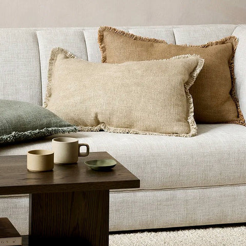 Three fringed lumbar cushions by Baya, seen on a stylish couch
