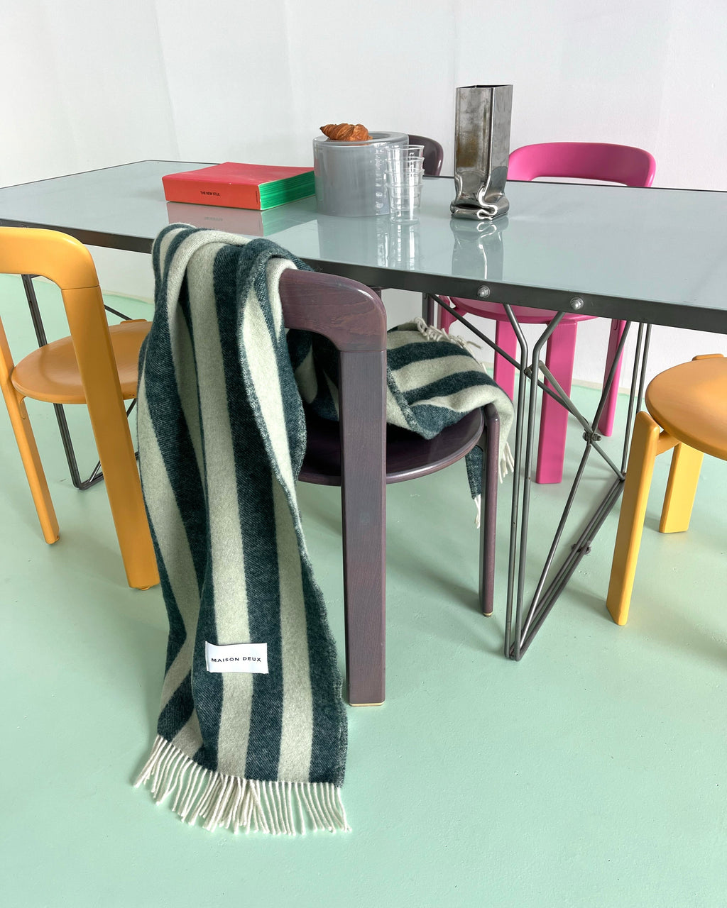 A sage and forest green wool throw blanket draped over a chair in a modern, stylish and vibrant dining room. 
