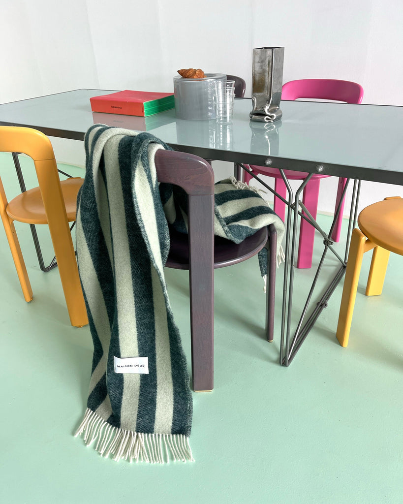 A sage and forest green wool throw blanket draped over a chair in a modern, stylish and vibrant dining room. 