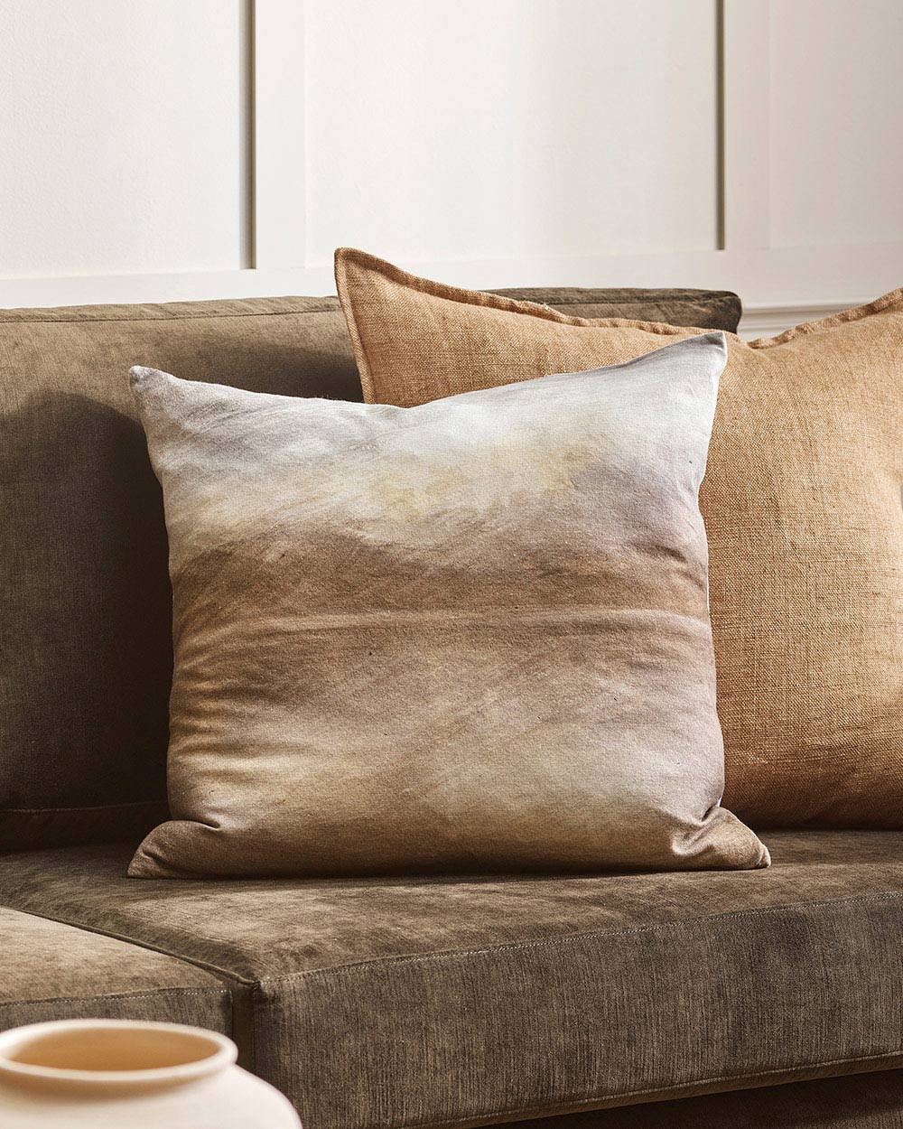 A close up image of an earth toned couch with a stunning feature cushion depicting a hand-painted abstract landscape. 