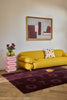 Modern living room with a yellow sofa, pink side table, and Marimekko Unikko floral patterned rug in burgundy / merlot colour