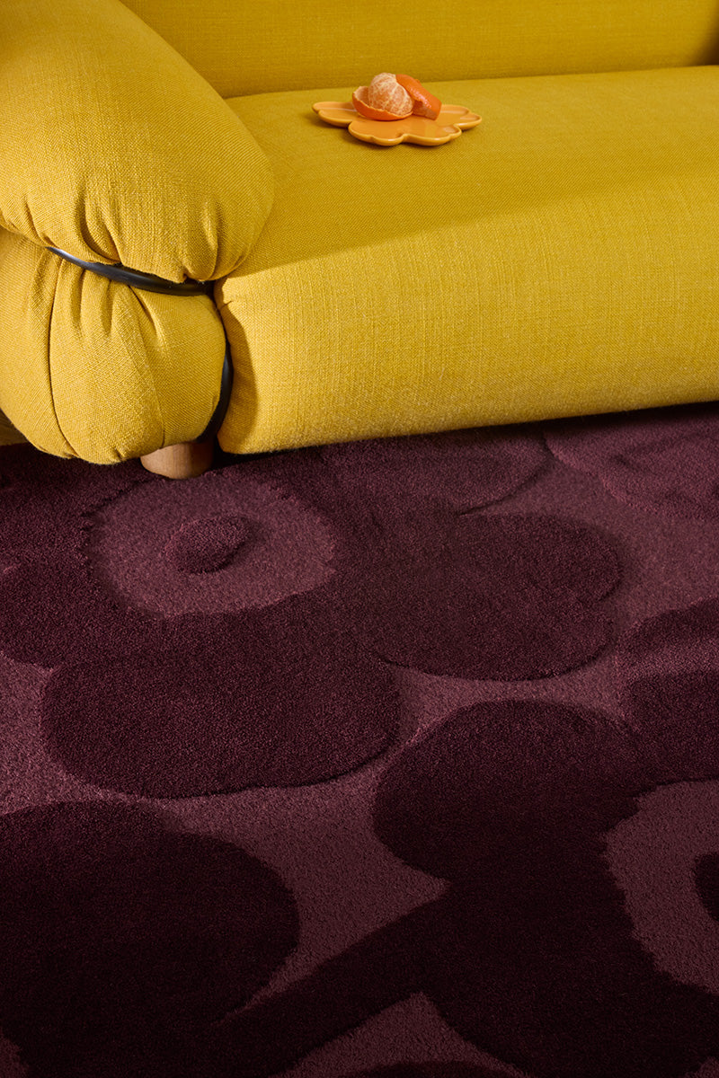 Marimekko Unikko floral patterned rug with deep burgundy flowers and a yellow couch