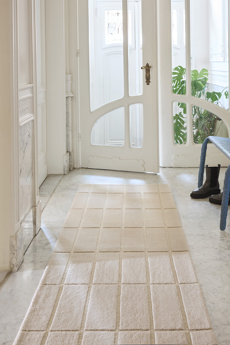 A Marimekko grid patterned runner rug in a neutral creamy white shown in a stylish hallway entrance