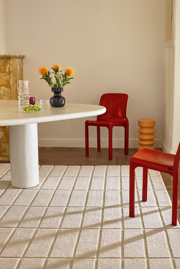 A Marimekko grid patterned rug in a neutral creamy white featuring in a stylish dining room setting