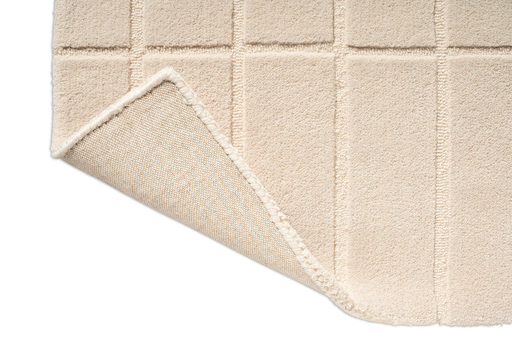A Marimekko grid patterned rug in NZ wool and in a neutral creamy white folded over to show the backing