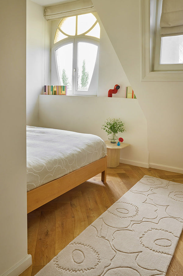 Bedroom with wooden bed, white bedding, and a Marimekko runner rug in a creamy white with a subtle graphic cut into it