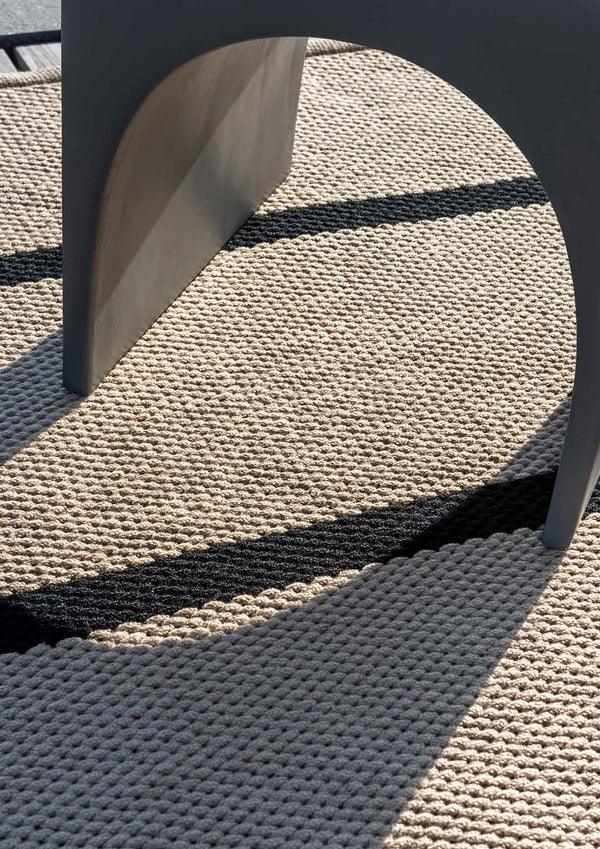 A close up of a premium outdoor rug by Brink & Campan featuring a charcoal black and beige stripe