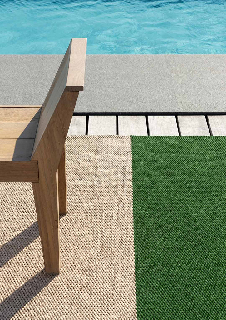 A summer poolside scene featuring a premium outdoor rug with a green and beige stripe, designer rug by Brink & Campman