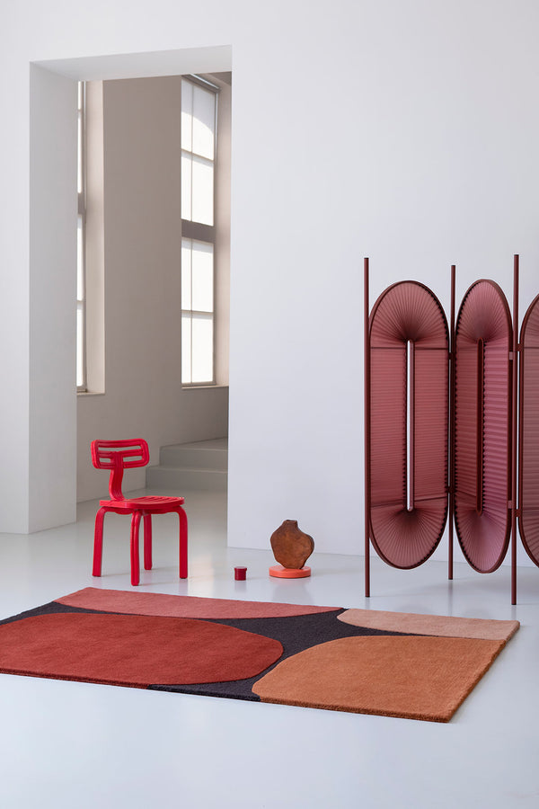 A modern floor rug featuring red tones and graphic shapes, shown in a contemporary minimalist living space