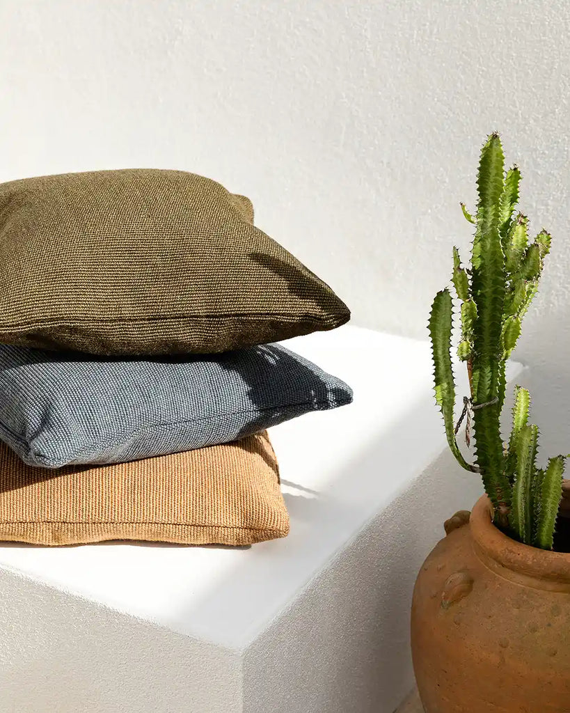 Stack of outdoor cushions made from PET recycled plastic bottles. Colours blue, olive green and a warm , light brown.