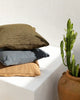 Stack of outdoor cushions made from PET recycled plastic bottles. Colours blue, olive green and a warm , light brown.