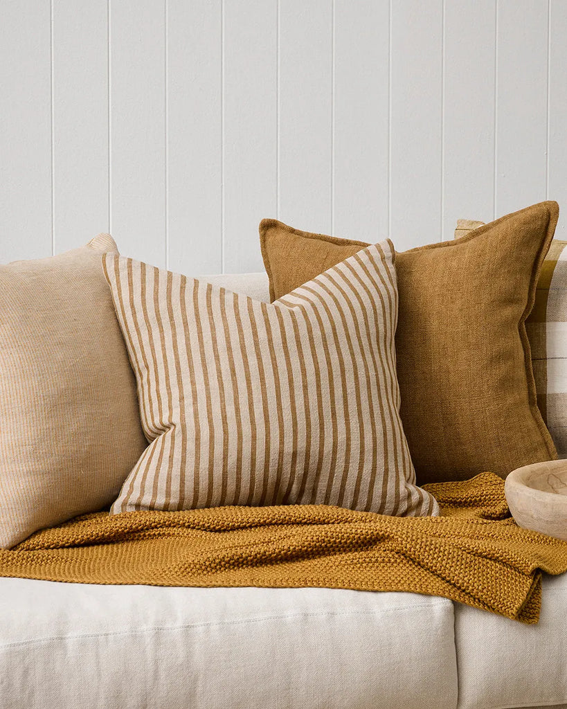 A modern lounge setting featuring a close up of the Baya 'Spencer' linen cushion featuring a natural linen and ochre stripe