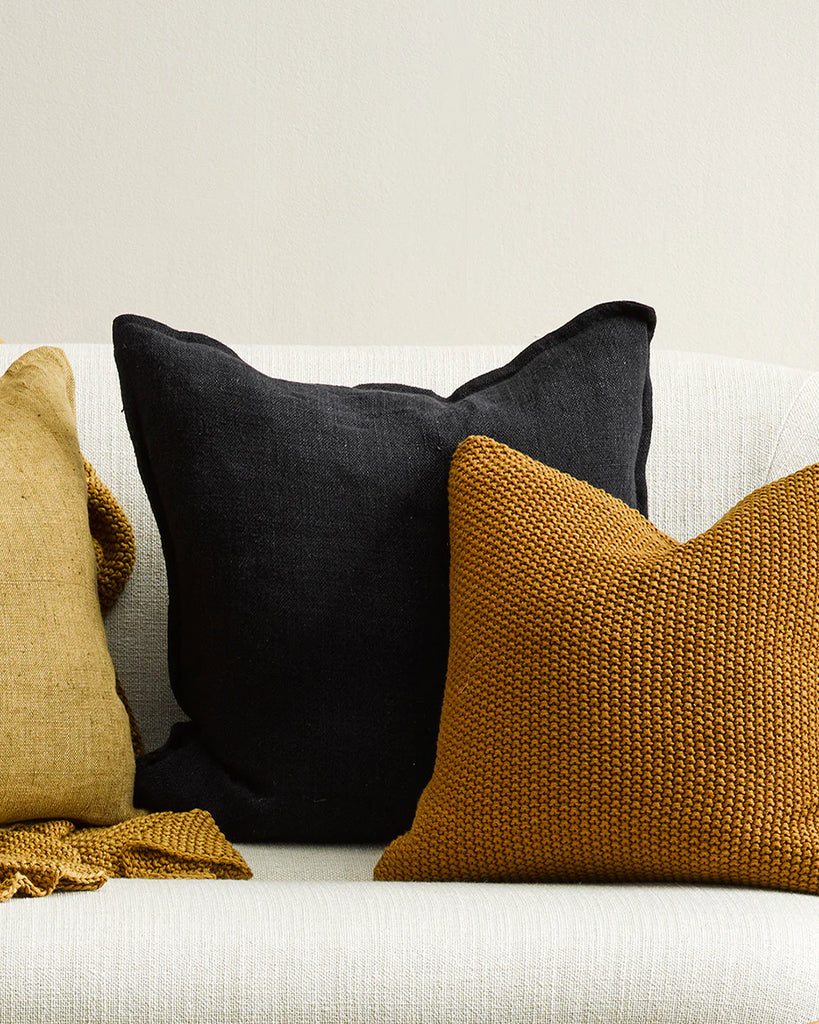 The black Baya flaxmill  linen cushion behind some warm toned cushions