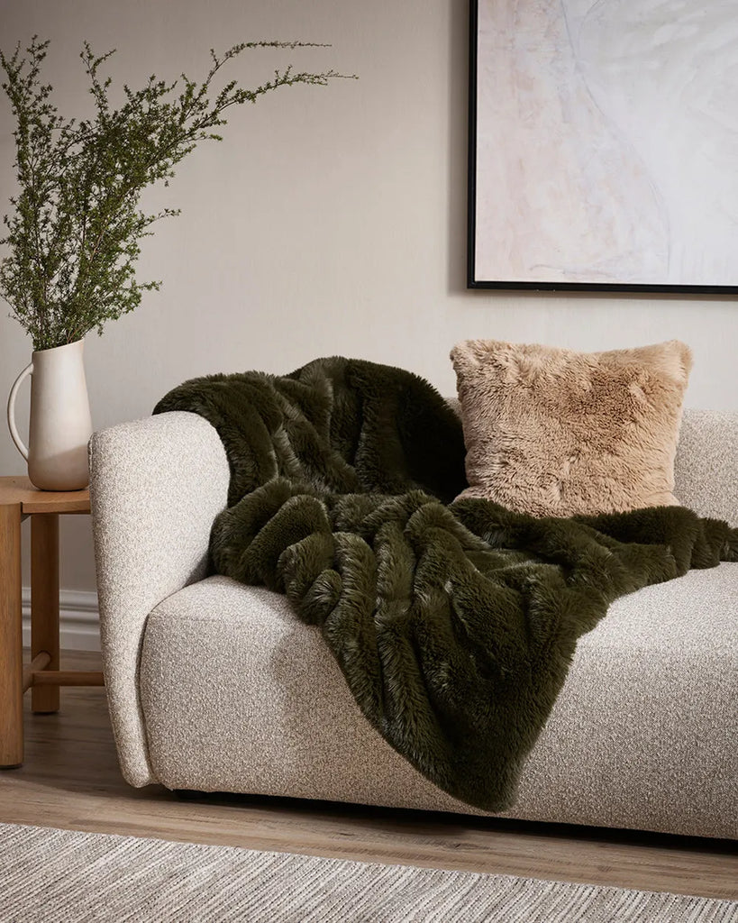 Pele Faux fur thrpow blanket by Baya, in a dark seaweed green colour, draped over a couch in a modern living room