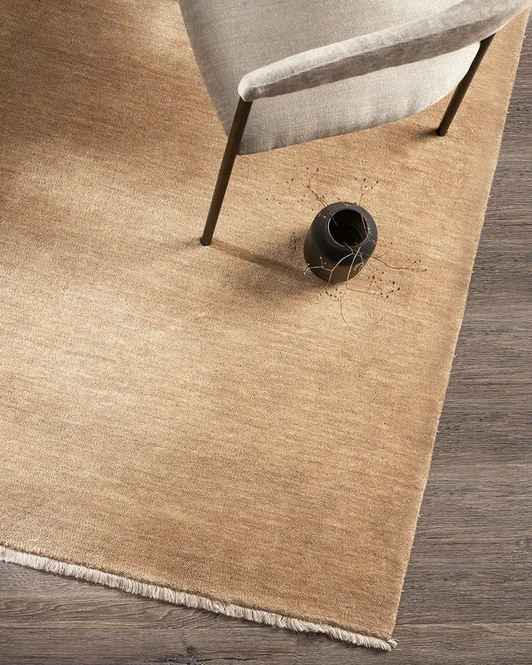A soft caramel-toned wool floor rug - the Baya Sandringham Putty - seen fromabove under a chair
