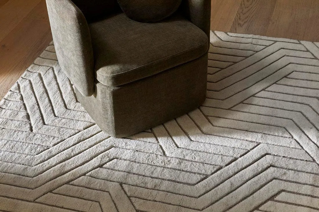 A stylish, cream/ivory wool floor rug featuring a striking geometric design, under a chair in a modern room