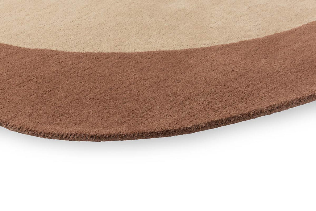 Close up of the edge of a warm brown and beige toned rug, with a curving finish. 