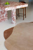 A handtufted rug in warm brown tones with an irregular, organic shape. Styled in a modern dining room. By Brink and Campman