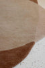 Close up image of the weave of an organically shaped rug, in warm brown tones. By Brink and Campman