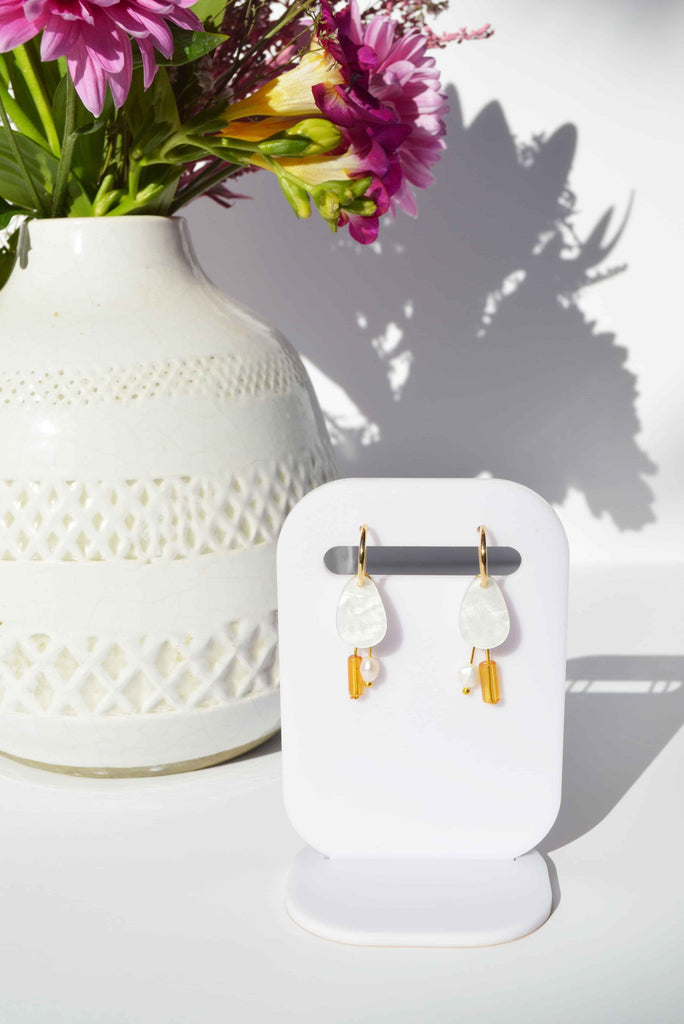 White earrings with gold findings, amber beads and a freshwater pearl, displayed on a stand