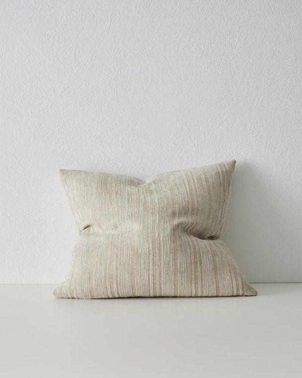 A beige textured pillow by Weave Home sits against a white wall on a white surface.