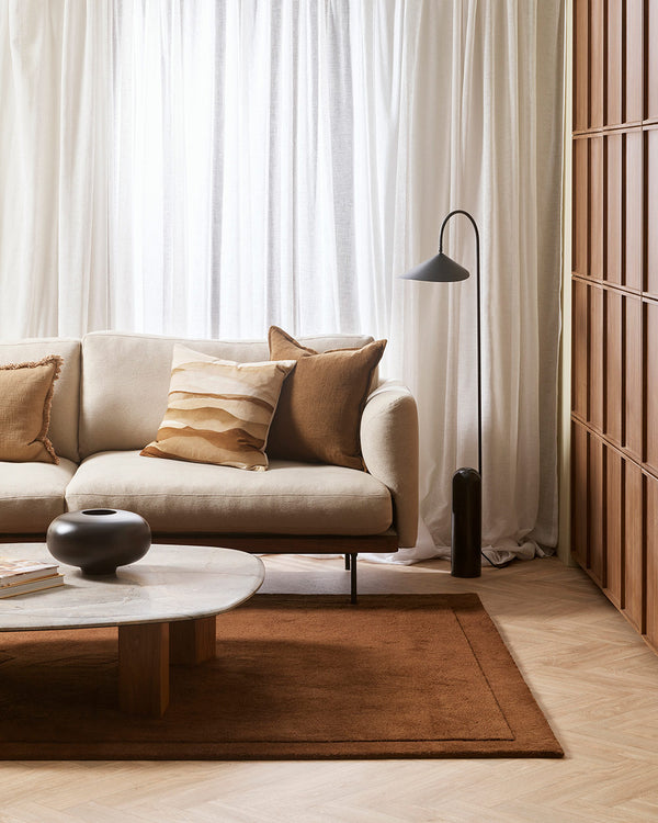 A stylish living room decorated in warm brown and cream tones, with a feature pillow in shades of cream and tan, patterned with sand dunes. By Baya. 