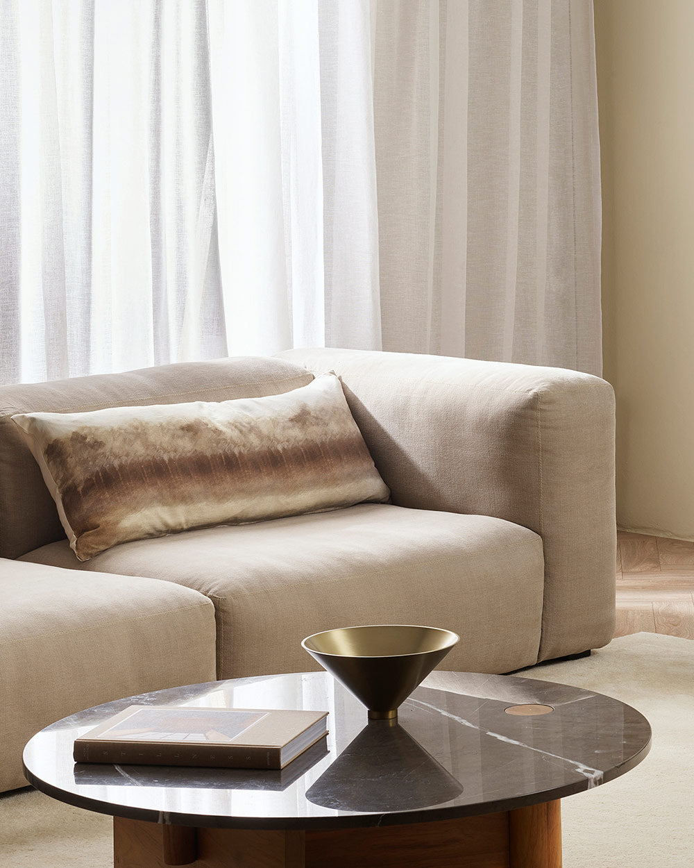 A couch featuring a stunning long lumbar cushion with a hand-painted abstract rendition of a treeline, in warm brown and sienna tones. By Baya