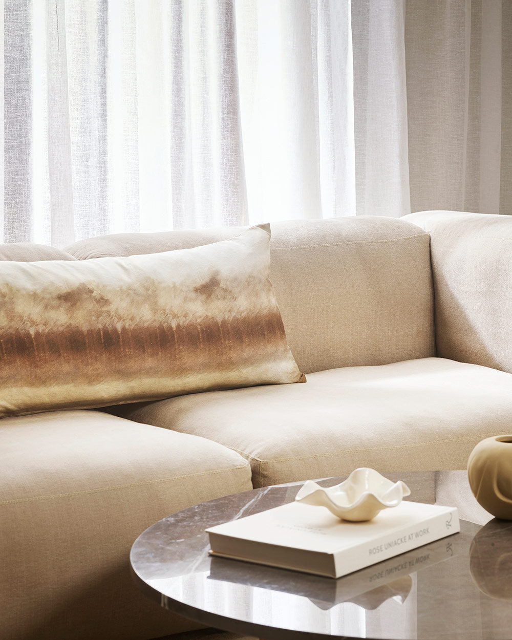 A couch with the Woodhill Long Lumbar cushion on it, featuring an abstracted image of trees and forest, rendered in soft browns and creams. By Baya. 