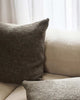 A soft woven textural cushion in tones of deep rosemary green on a cream toned couch, by Baya. 