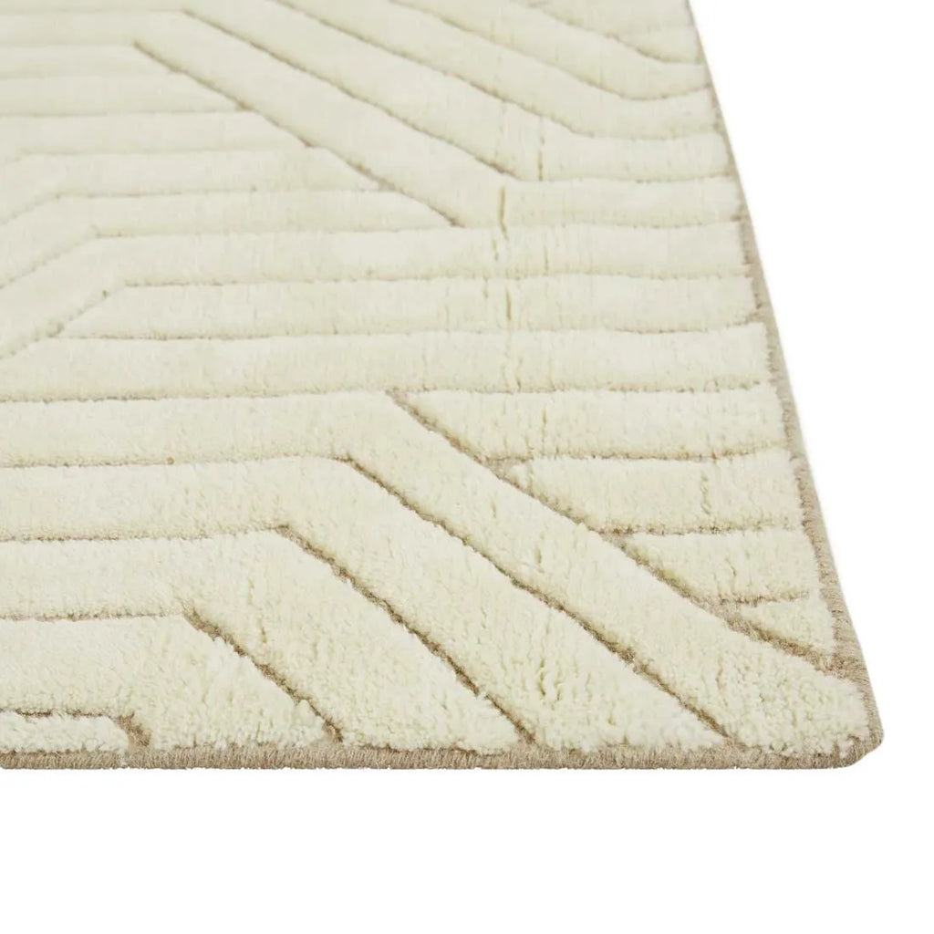Corner of a cream/ivory wool floor rug featuring a striking geometric design