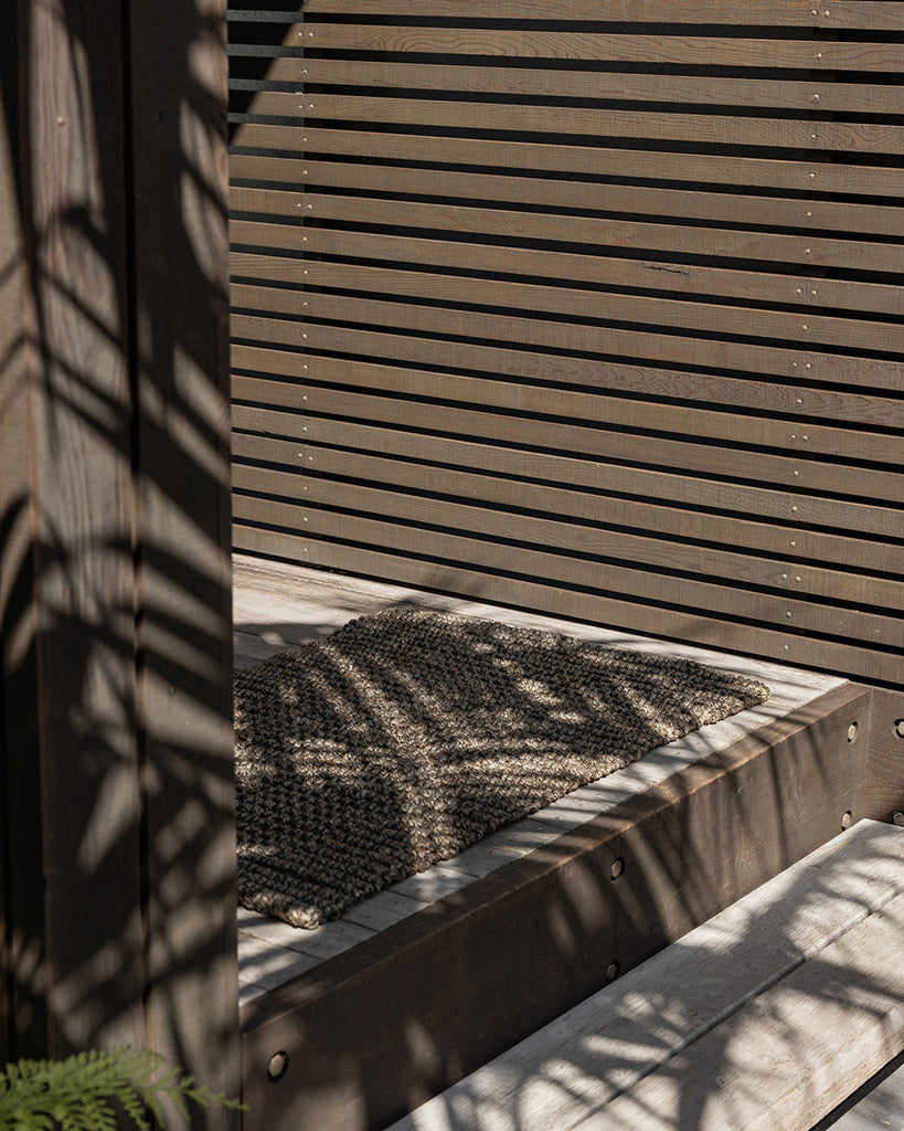 An entranceway with a doormat made with natural dark jute fibres by Baya. 