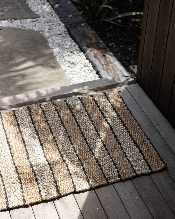 An entranceway with a striped doormat in different tones of natural jute, handwoven and designed by Baya. 