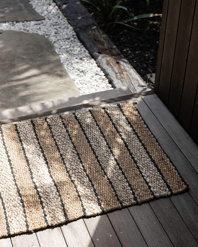 An entranceway with a striped doormat in different tones of natural jute, handwoven and designed by Baya. 