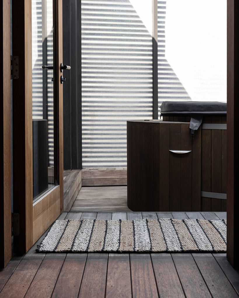 A doorway with an entrance mat made of striking striped natural handwoven jute fibres, by Baya. 