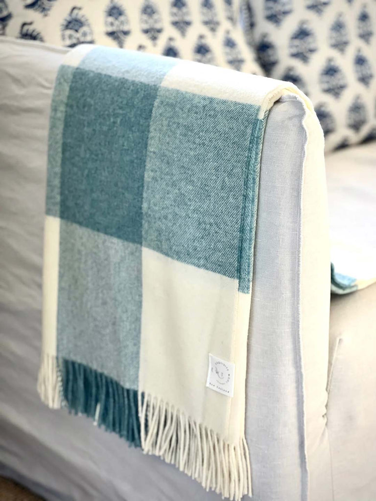 Pure NZ wool throw in cream and blue check plaid, by Exquisite Wool Traders, folded and draped over a chair