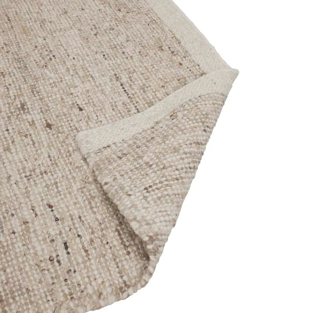 Close up of the corner of a textural woolen rug, in shades of cream, honey brown and light beige, with subtle colour shifts by Soren Liv NZ and Globe West. The edge of the rug is flipped up to show the underside. 