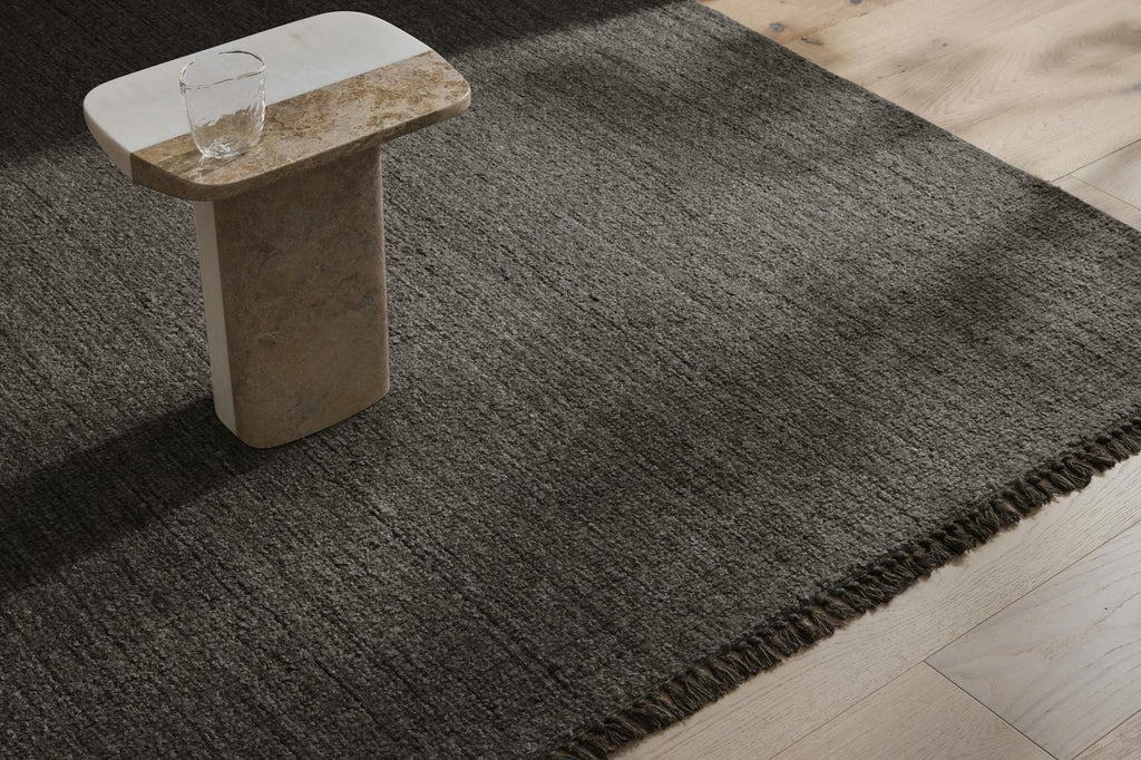 The 'Puglia' floor rug by Weave Home, in colour 'Pigeon" - a deep cool-toned brown - seen on floor, highlighting the fringed edge.