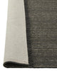 The 'Puglia' floor rug by Weave Home, in colour 'Pigeon" - a deep cool-toned brown, with edge folded up to reveal the backing.