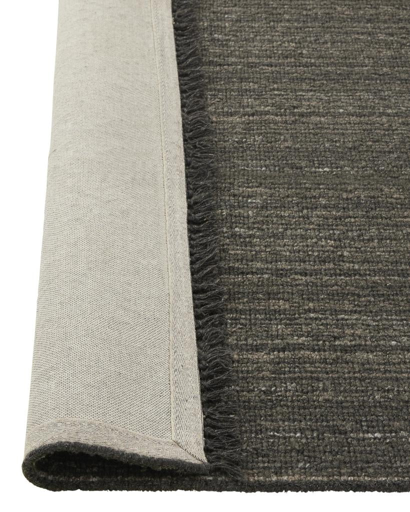 The 'Puglia' floor rug by Weave Home, in colour 'Pigeon" - a deep cool-toned brown, with edge folded up to reveal the backing.