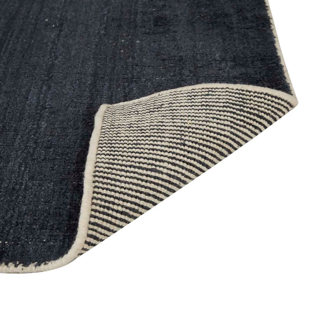 Close up of the weave of a dark blue wool blend floor rug with corner folded to reveal underneath