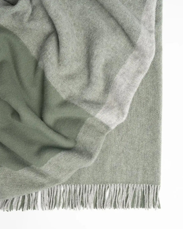 A soft green and grey wool throw in a large size, with fringe