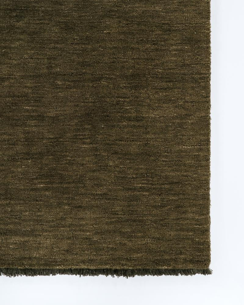 A corner image of a 100% wool moss green floor runner with a small fringed edge.