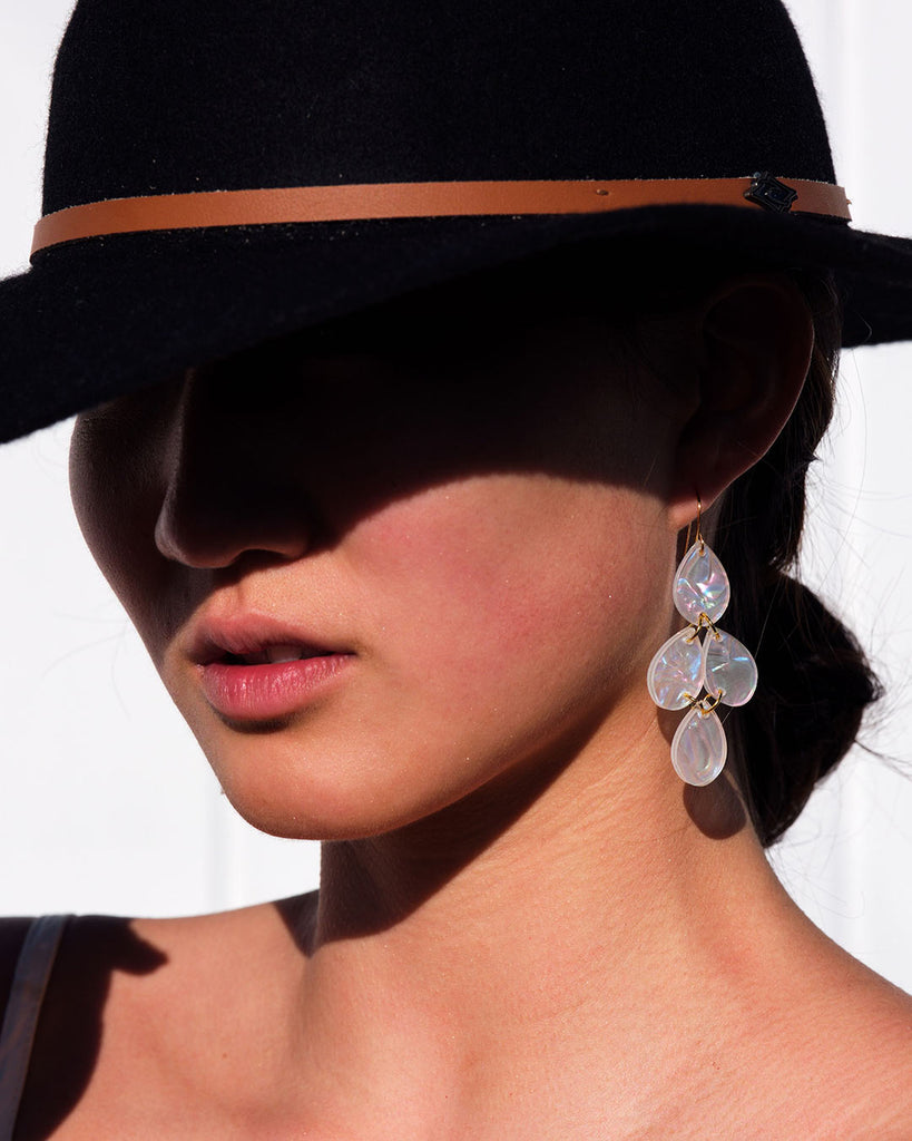 A woman in a hat wearing pearlescent dangle earrings by Hagen + Co
