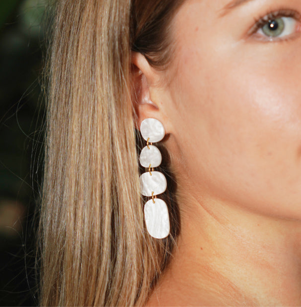 Close up of a model wearing white pearl coloured acrylic dangle earrings by Hagen + Co