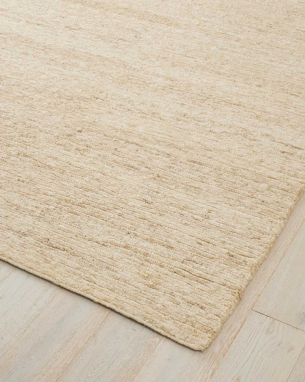 The corner of a cream toned pale jute handwoven rug. 