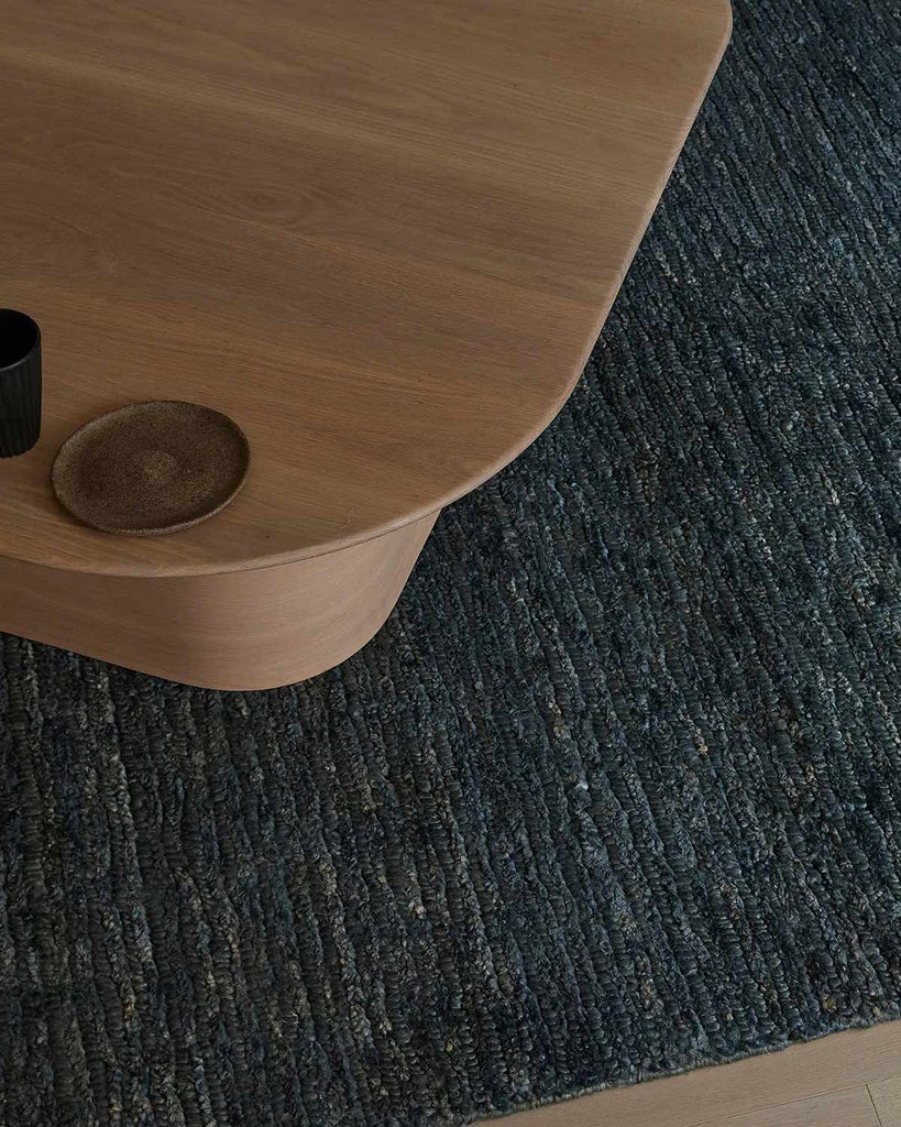 A coffee table on top of a highly textured deep blue jute floor rug with an alternating cut and loop pile weave. 