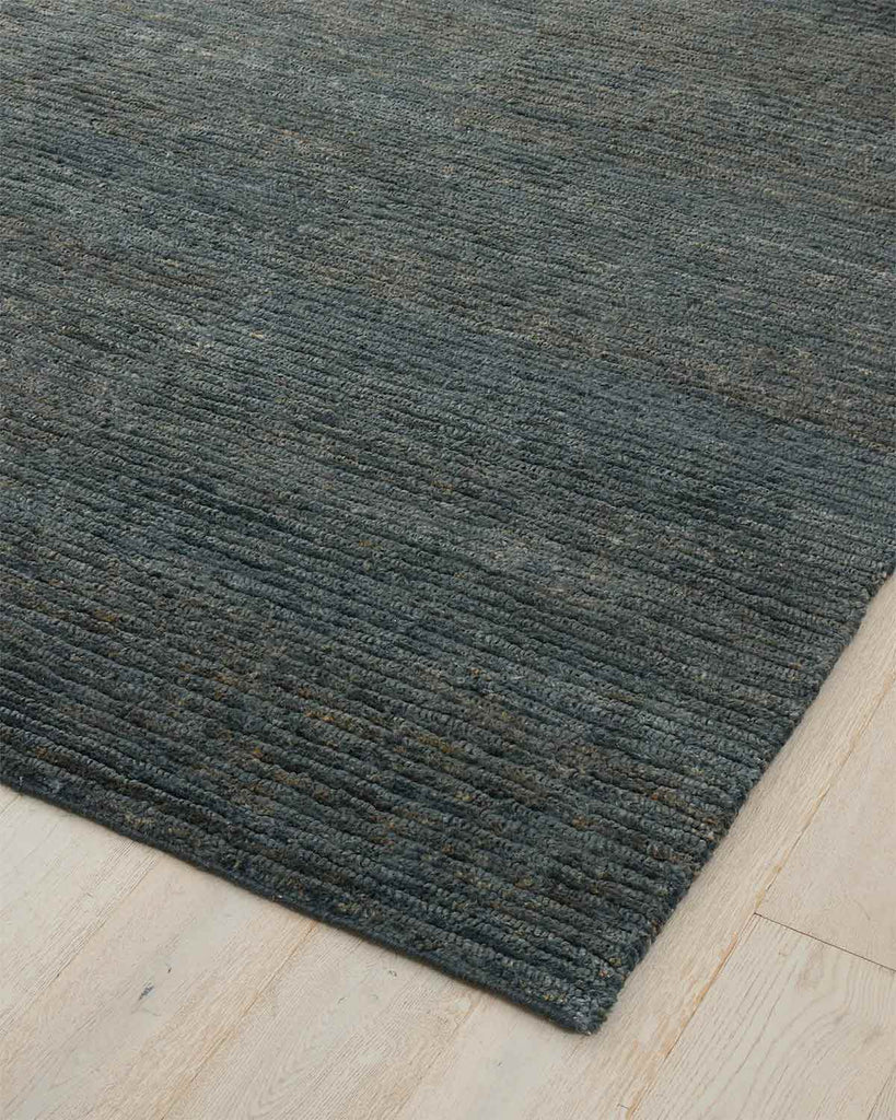 A blue floor rug woven from 100% jute fibres in an alternating looped and cut style weave. 
