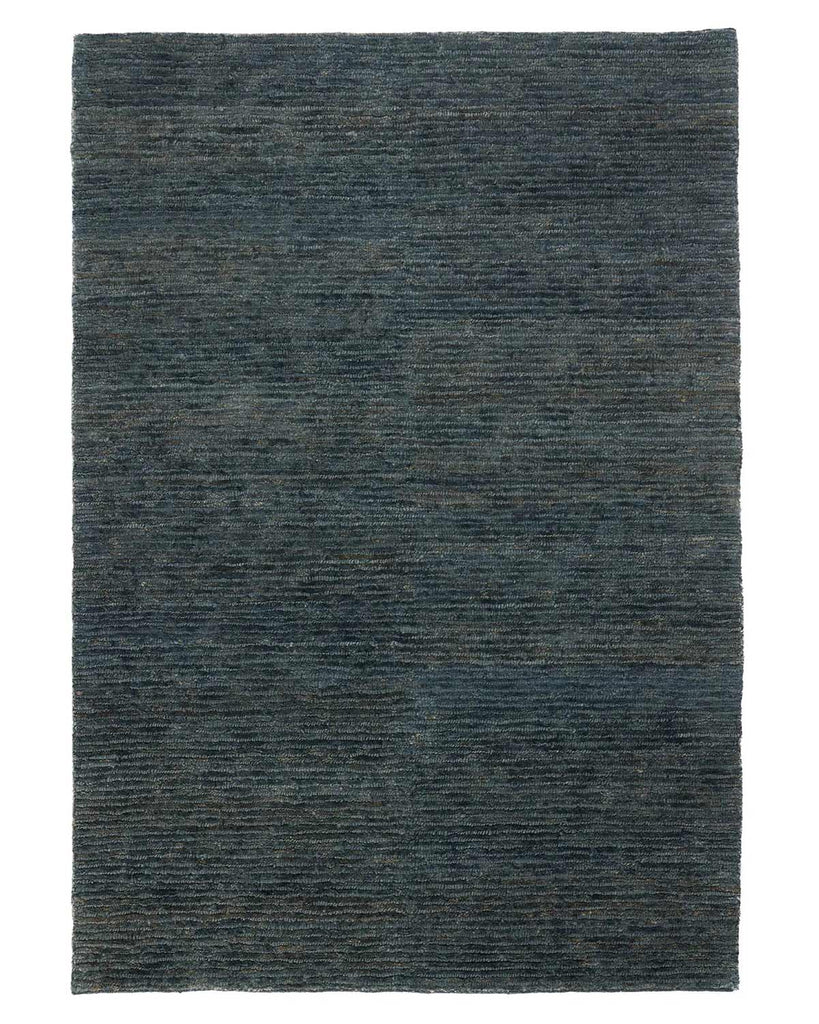 A full image of a muted deep blue-green jute floor rug with dynamic texturing and handwoven detailing. 