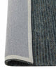 The corner of a blue jute floor rug with the edge flipped up to reveal the durable cotton backing. 