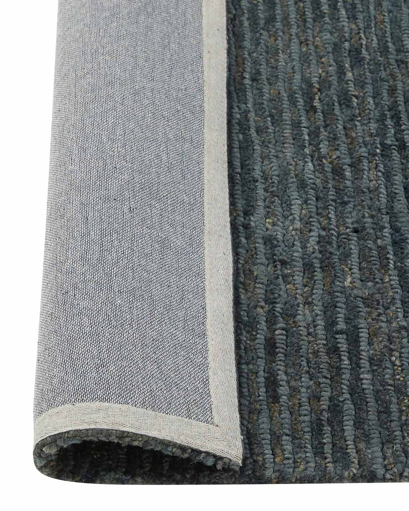 The corner of a blue jute floor rug with the edge flipped up to reveal the durable cotton backing. 